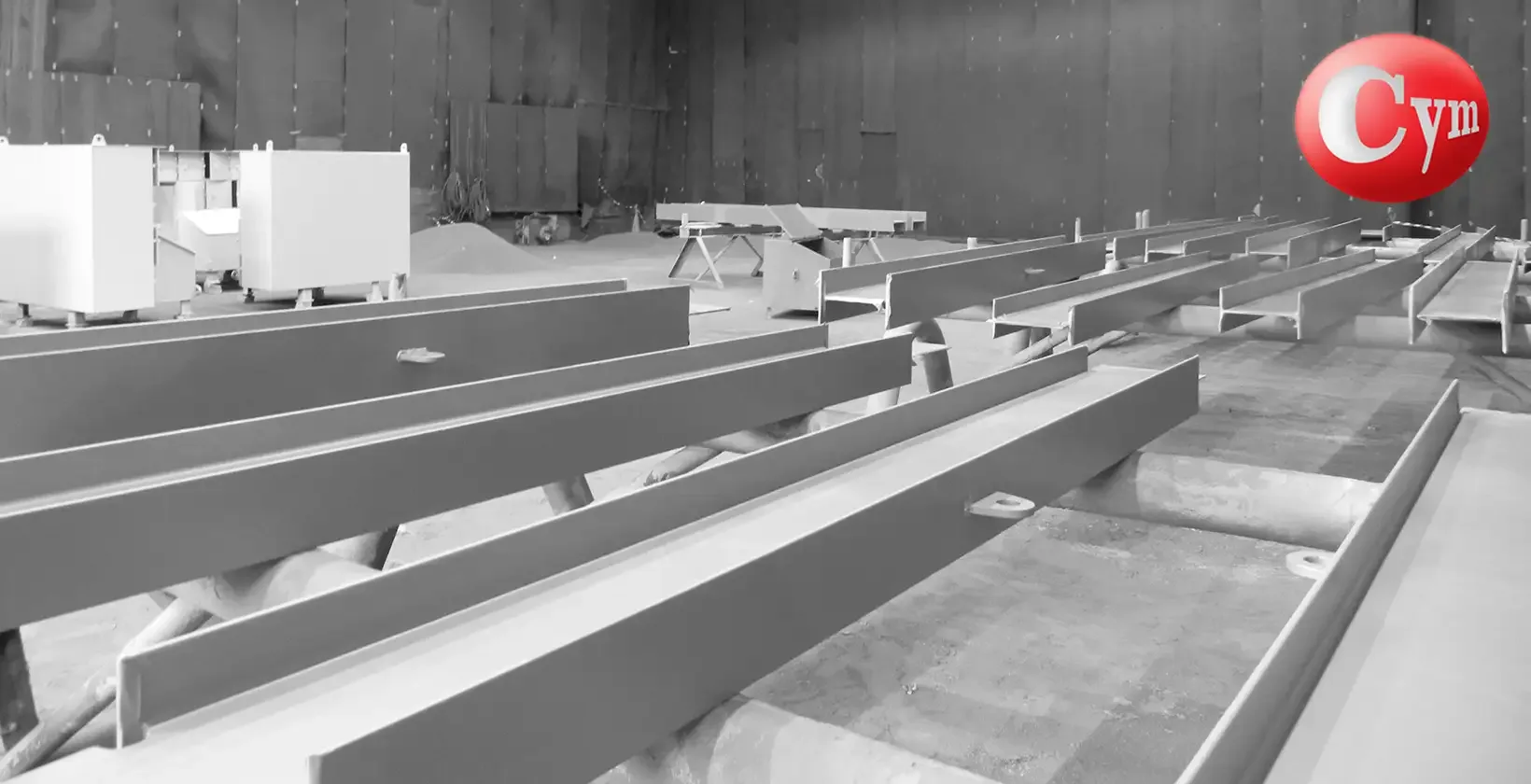 Interior cuarto jateamento Metalcym BrasFELS Brasil — perfis vigas aço sobre paletes indústria naval