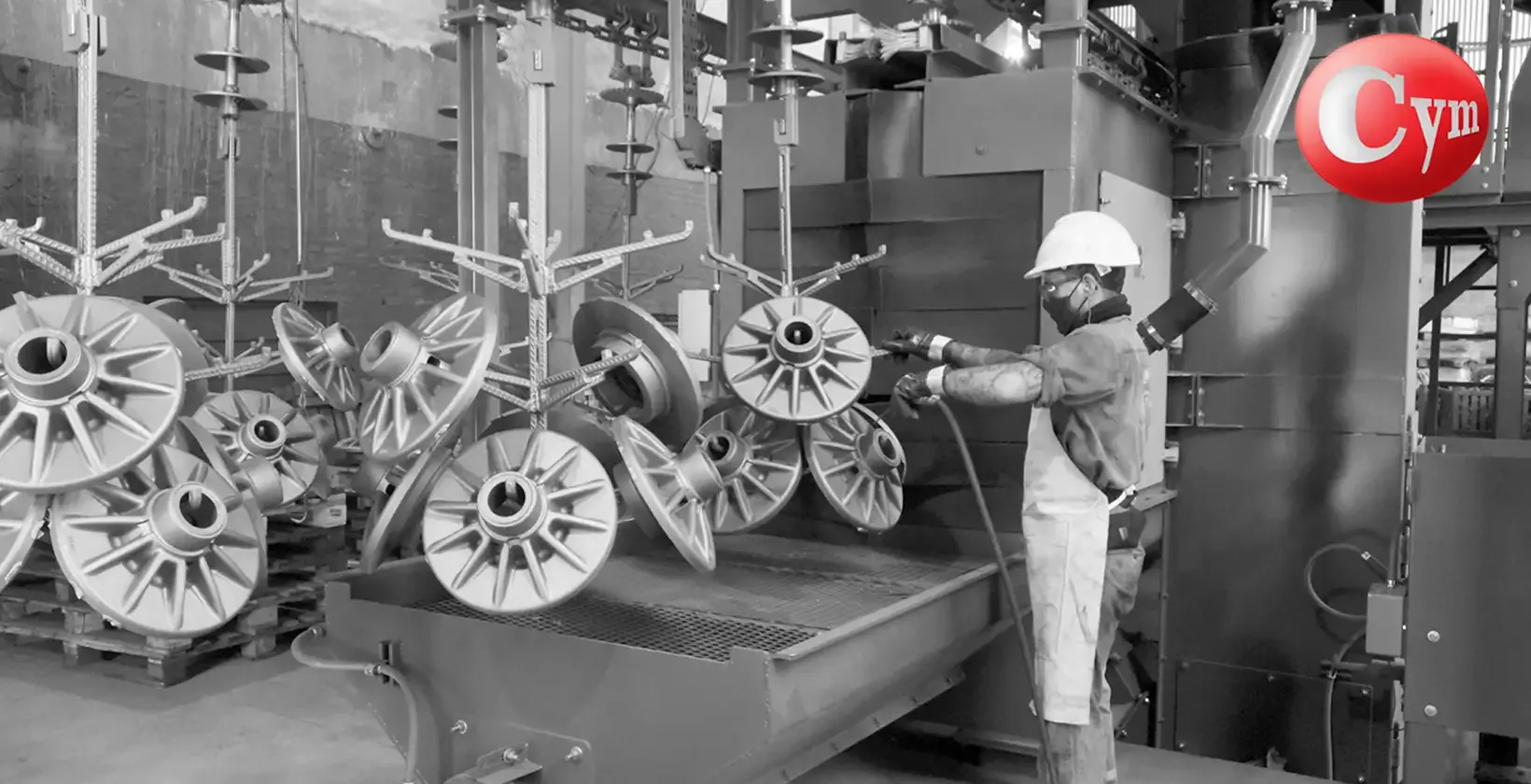 Túnel de jateamento de avanço contínuo CYM TUN 8x10 – operação de carga e descarga de peças fundidas em transportador aéreo de ganchos